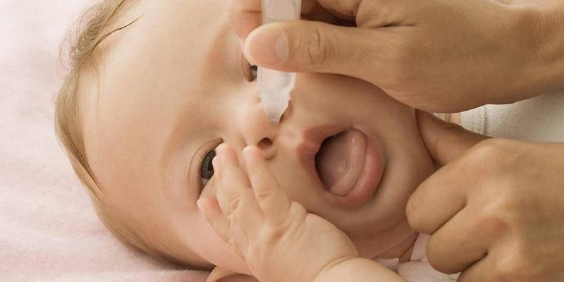 Hình ảnh một người lớn đang nhỏ nước muối sinh lý và hút mũi cho em bé
