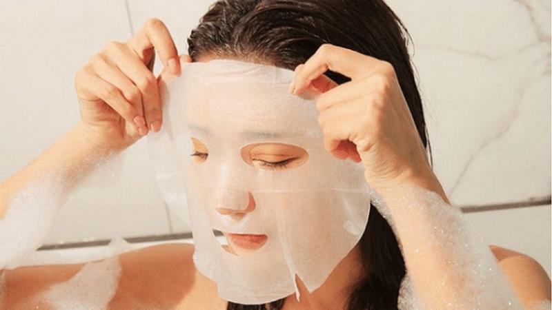 Một người phụ nữ nhẹ nhàng vỗ lên mặt sau khi gỡ mặt nạ giấy, giúp tinh chất thẩm thấu sâu vào da, thể hiện bước chăm sóc da sau mặt nạ
