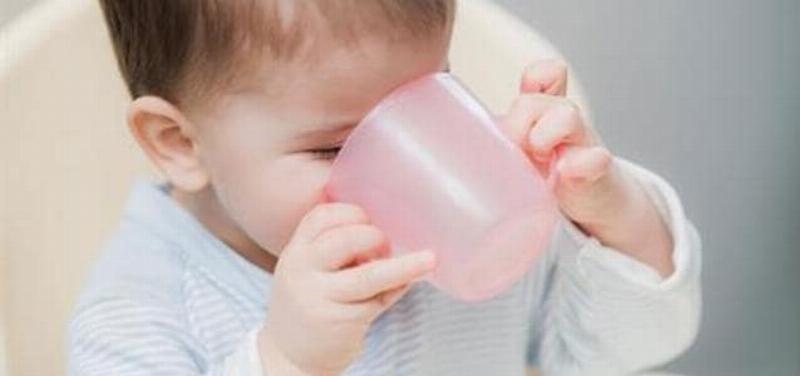 Một em bé đang vui vẻ uống nước từ cốc hoặc bình