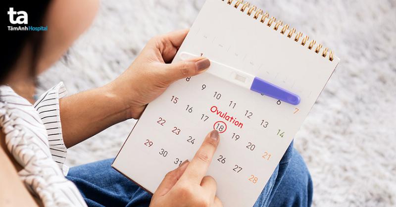 Người phụ nữ đang ngồi đối diện bác sĩ trong phòng khám, trên bàn có hồ sơ y tế, nhấn mạnh việc thăm khám chuyên khoa sau khi que thử thai hai vạch